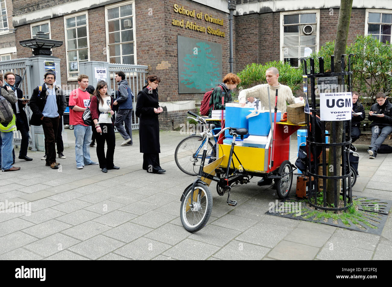 Man from the Hare Krishna Movement serving free food from a bicycle trailer to students and passers by, London England UK Stock Photo