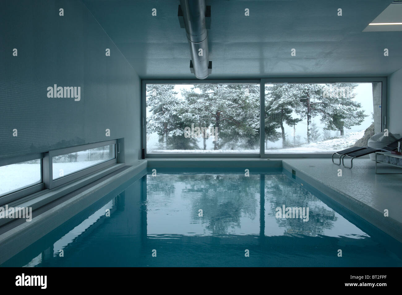 Indoor swimming pool in the winter with large window with a view to snow covered trees Stock Photo