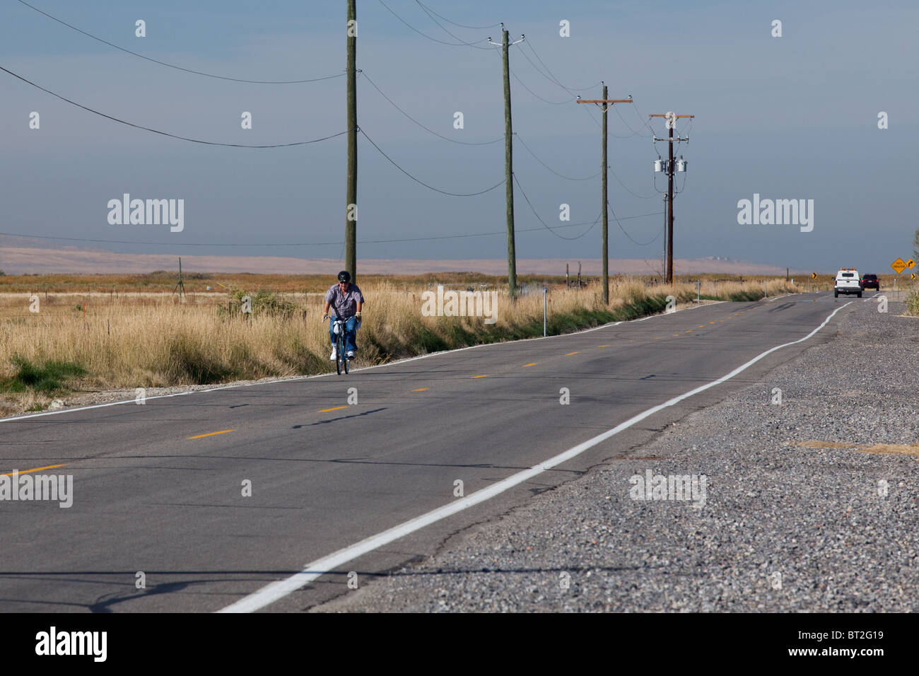 Older man riding a bicycle on a country road, in rural Utah Stock Photo