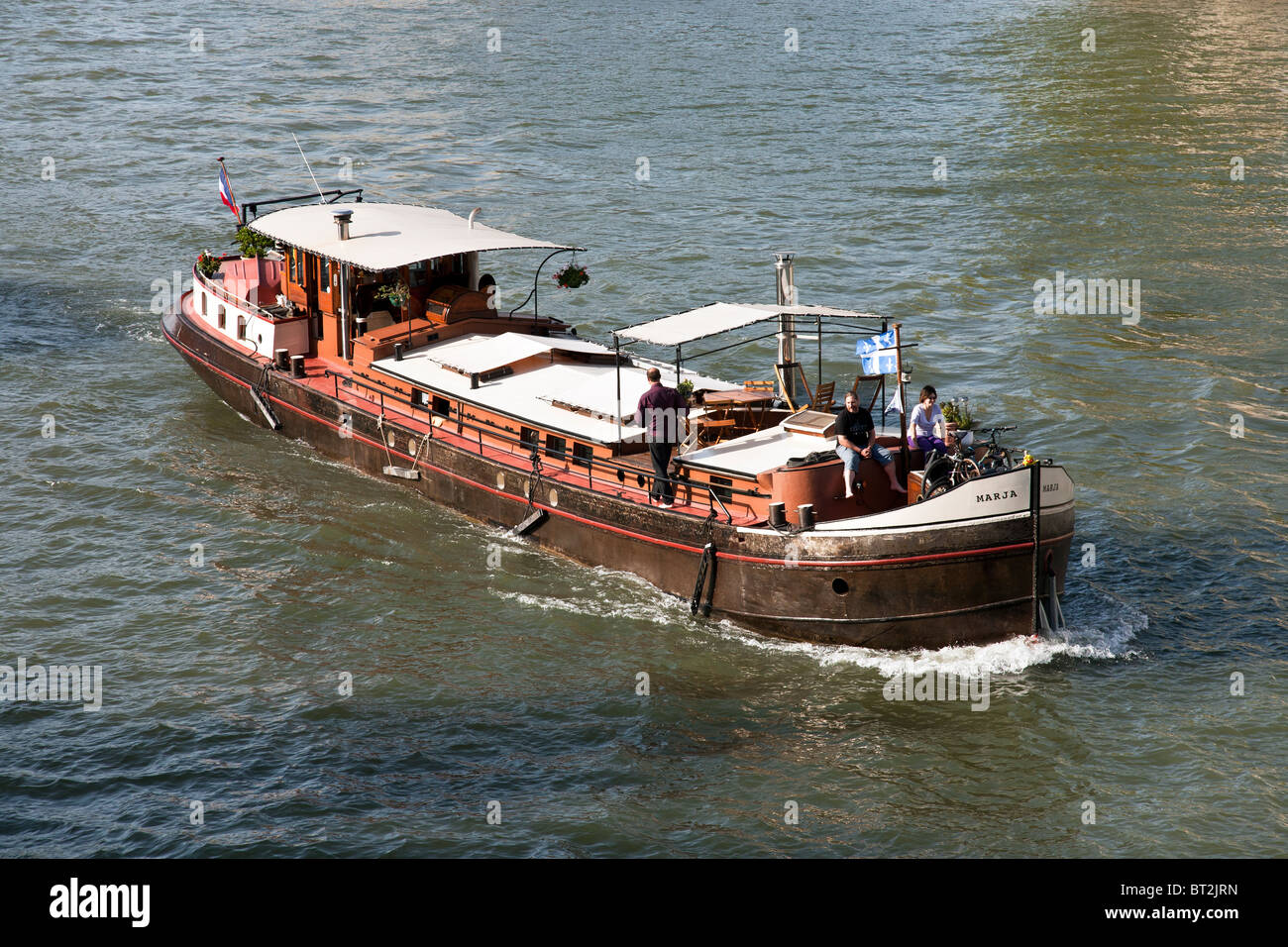 old barge converted to pleasure boat for hire plies blue green waters of Seine with happy couple sitting forward enjoying view Stock Photo