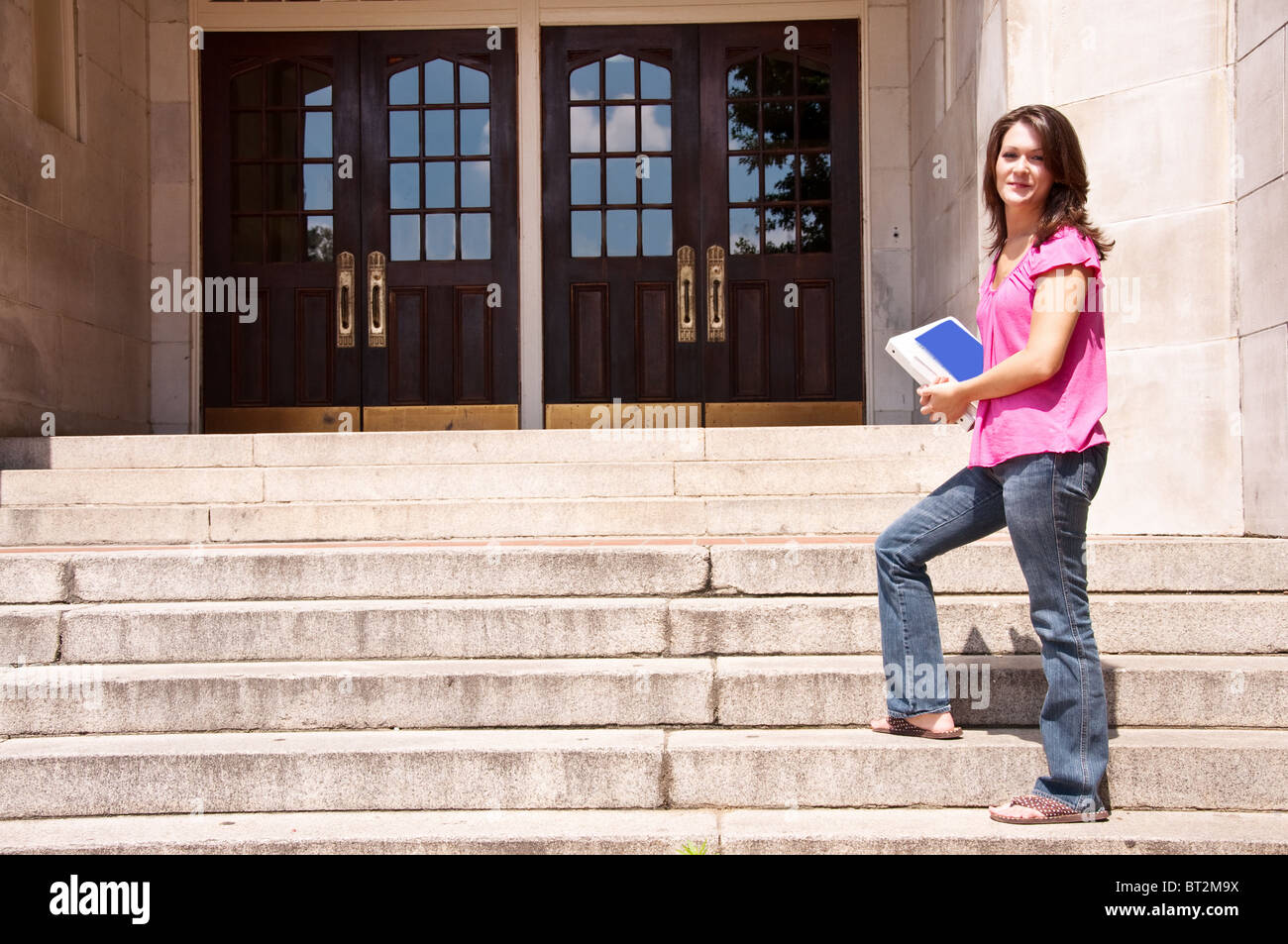 Female college student standing at front door of school with books in hand. Stock Photo