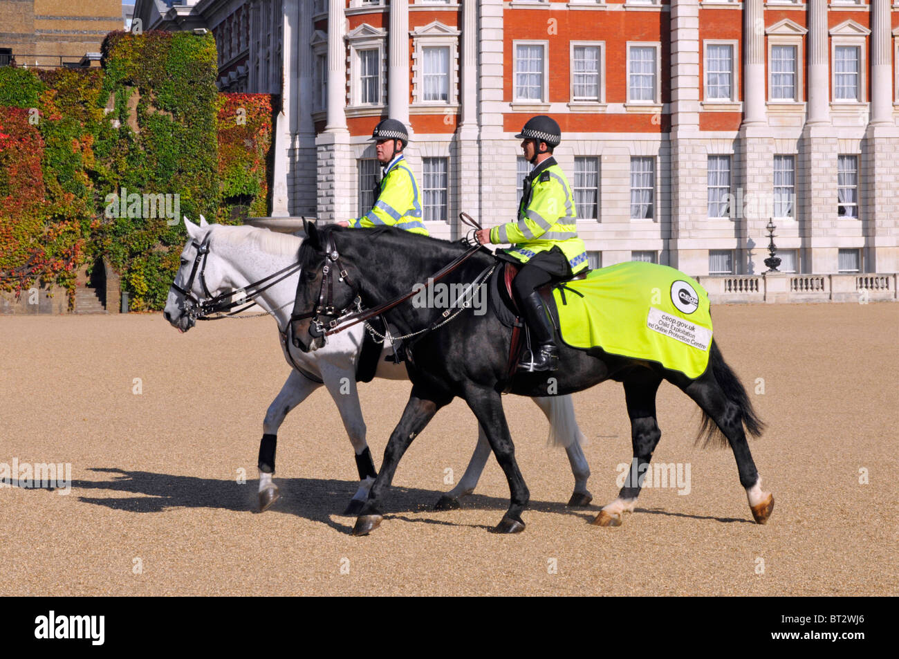 Horse Guards Parade Ground two mounted Metropolitan police officers riding bay & grey horses conspicuous high visibility clothing in London England UK Stock Photo