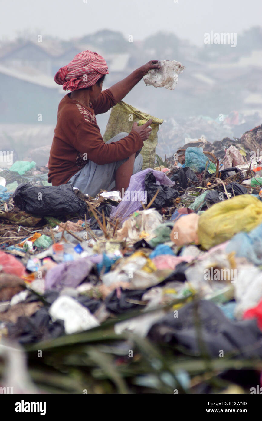 A woman worker living in poverty is looking through garbage for plastic bags at a dangerous and polluted trash dump in Cambodia. Stock Photo