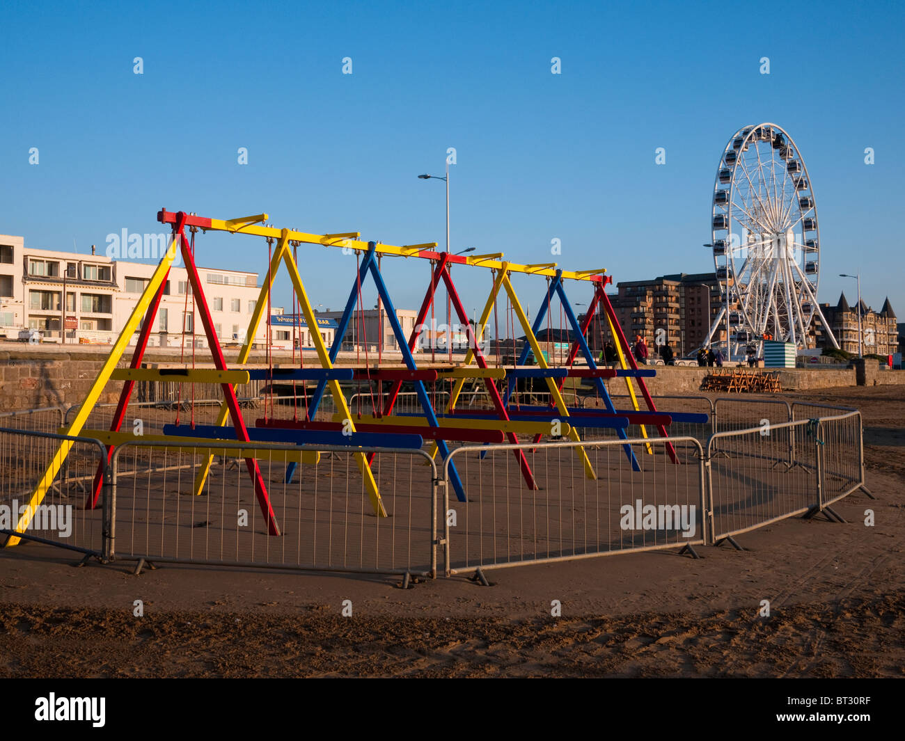 Children's swings and the Wheel of Weston on the seafront of Weston-super-Mare at sunset, North Somerset, England. Stock Photo