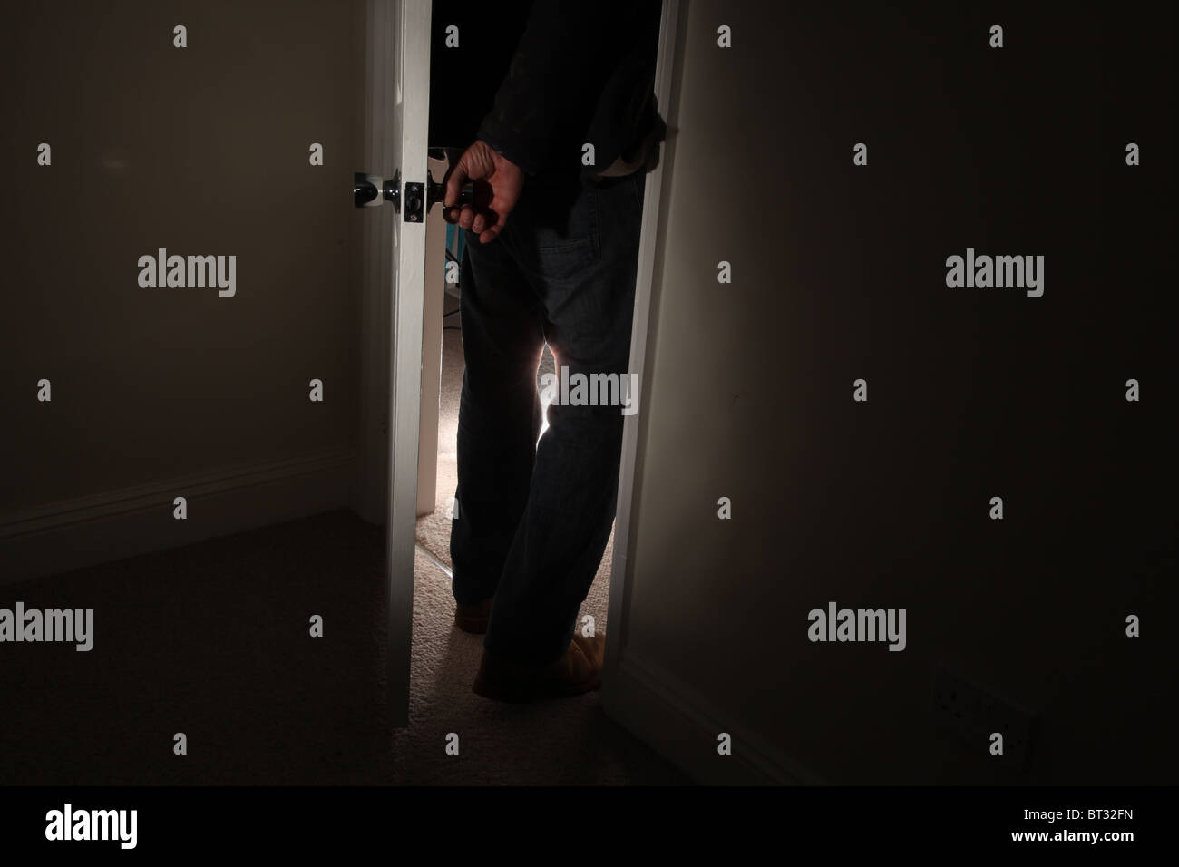 Man turning the handle opening a door entering a dark room Stock Photo