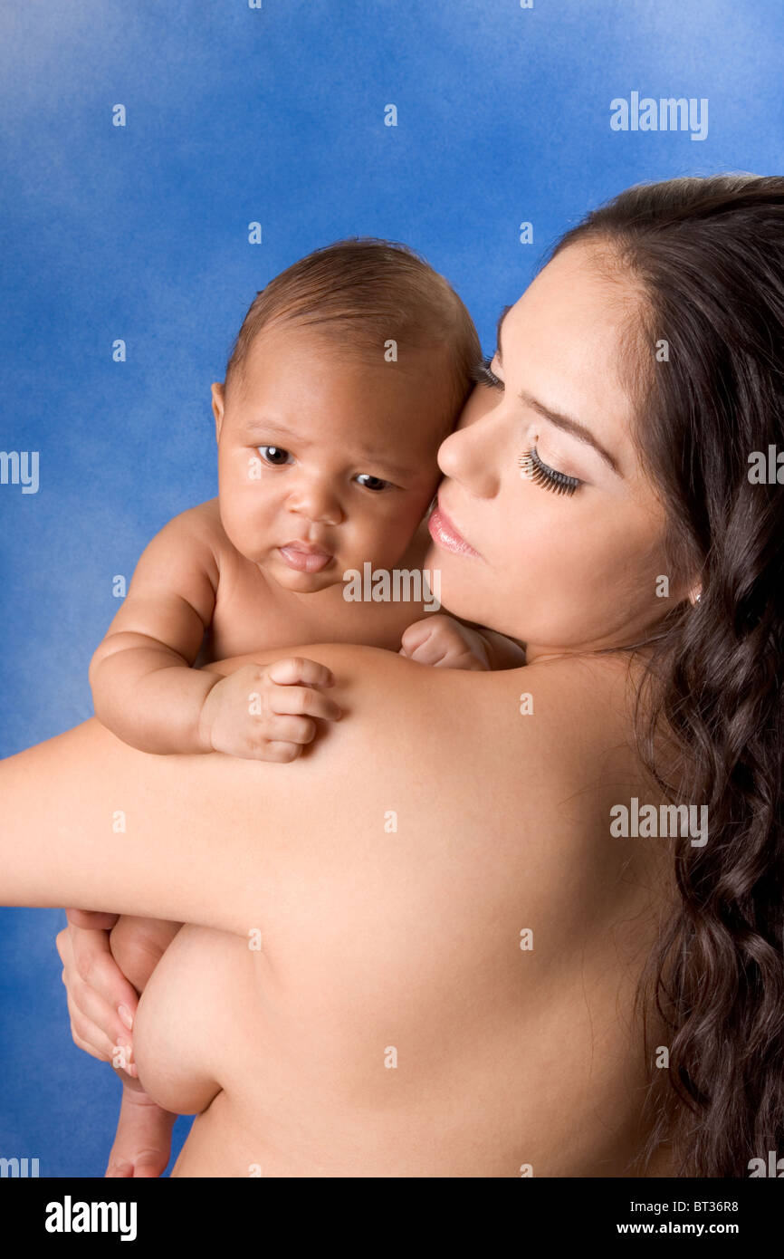 naked Hispanic mom holding her biracial mix of Hispanic and African American baby son against blue background Stock Photo