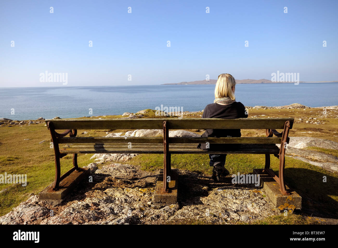 Woman sat on a bench looking out to sea Stock Photo
