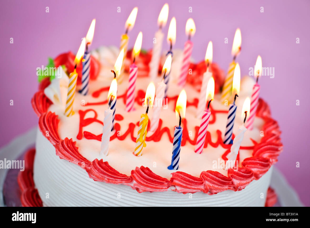 Birthday cake with burning candles and icing on pink background Stock ...