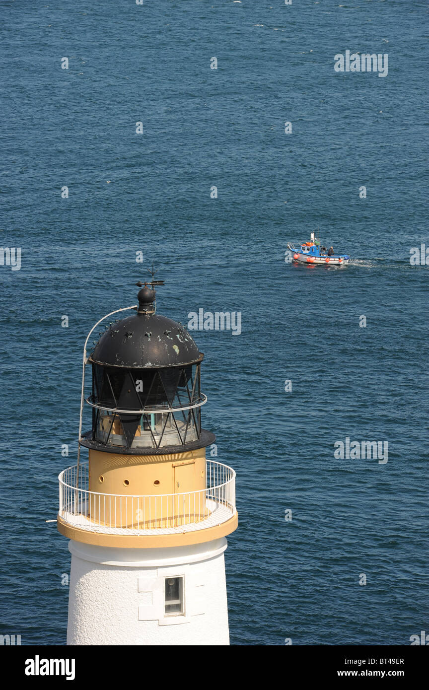 A small lobster fishing boat passes below Douglas Head Lighthouse, Isle of Man, UK Stock Photo