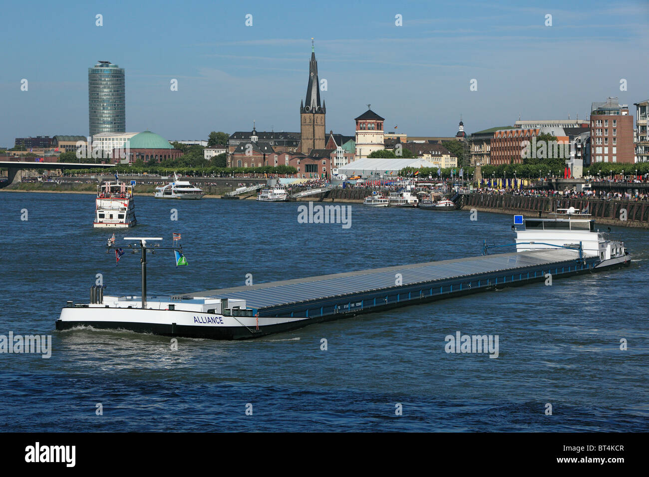 Frachtschiff auf dem Rhein vor der Rheinuferpromenade von Duesseldorf in Nordrhein-Westfalen mit Victoria-Hochhaus, Lambertuskirche und Schlossturm Stock Photo