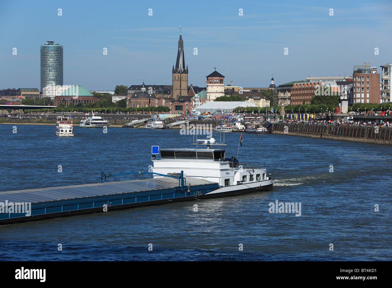 Frachtschiff auf dem Rhein vor der Rheinuferpromenade von Duesseldorf in Nordrhein-Westfalen mit Victoria-Hochhaus, Lambertuskirche und Schlossturm Stock Photo