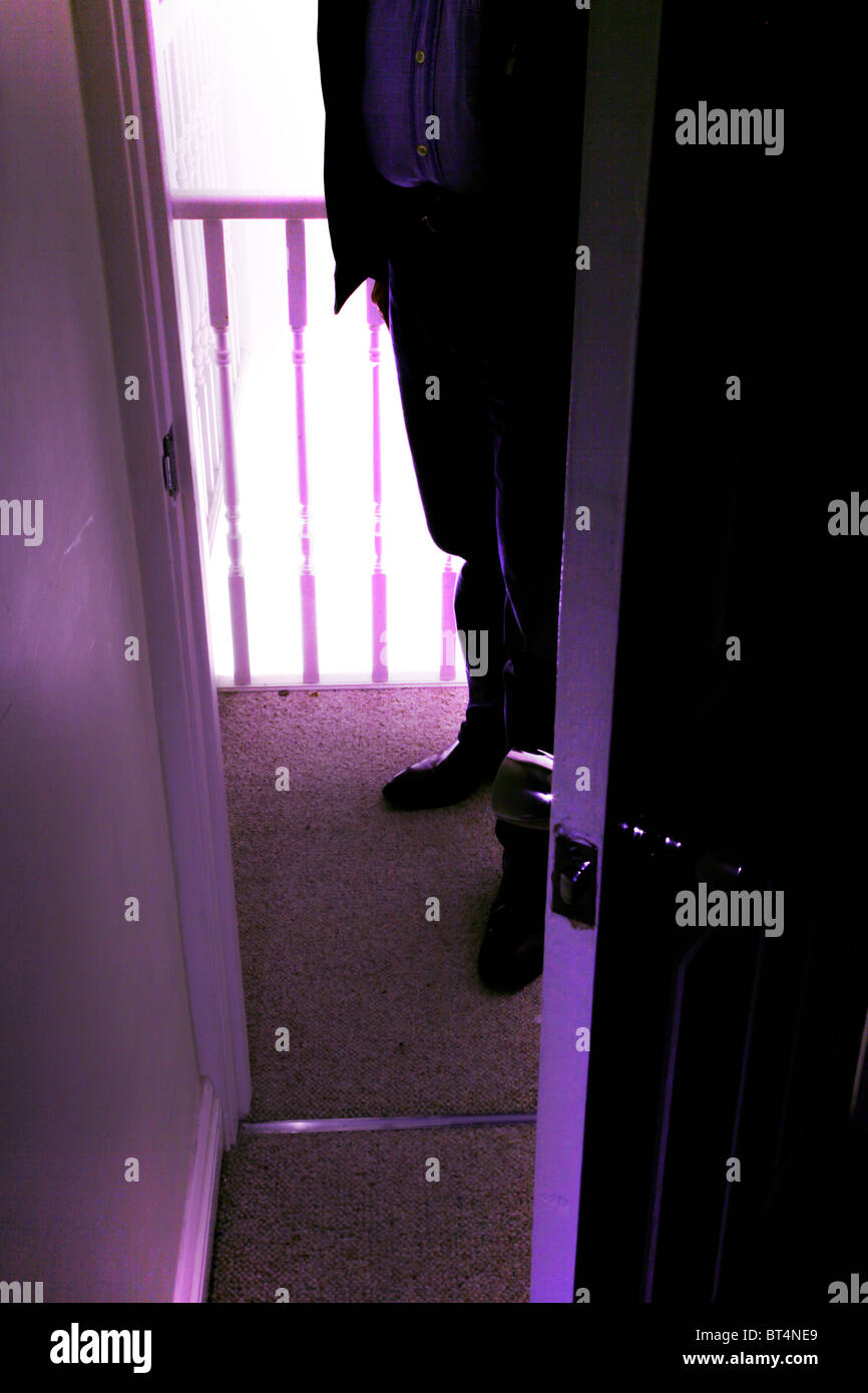 Man standing outside an open door to a dark room Stock Photo