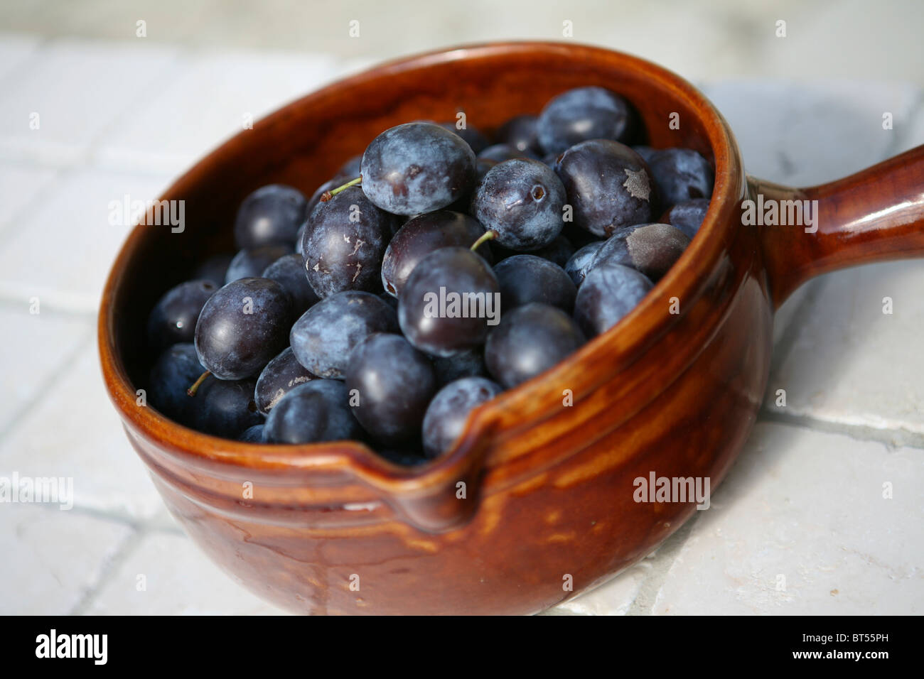 (Prunus domestica subsp. insititia) Freshly picked whole ripe damsons in a brown ceramic pot Stock Photo