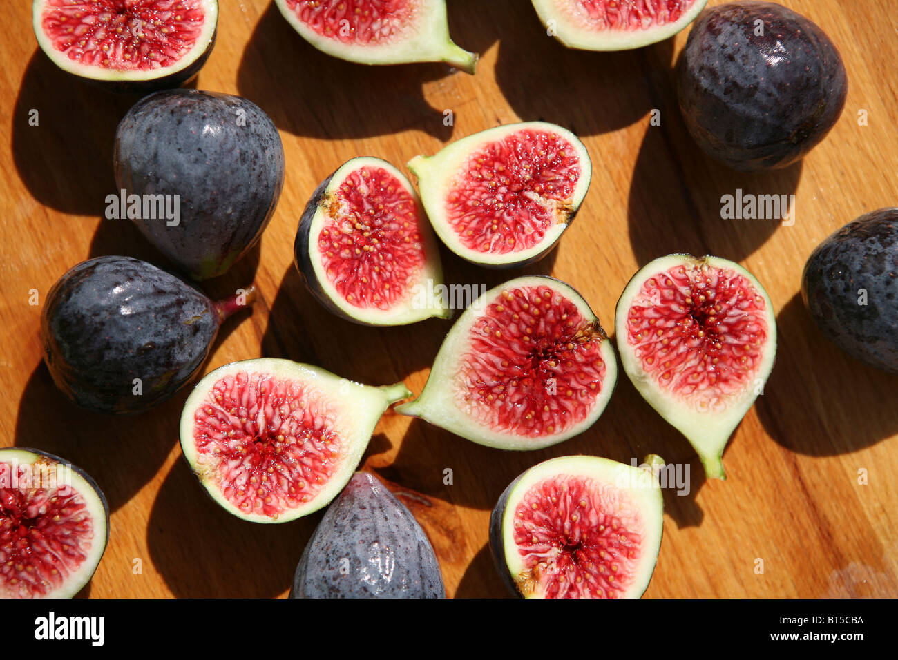 (Ficus carica) Halved and whole fresh figs on a wooden chopping board, outside, close up. Stock Photo