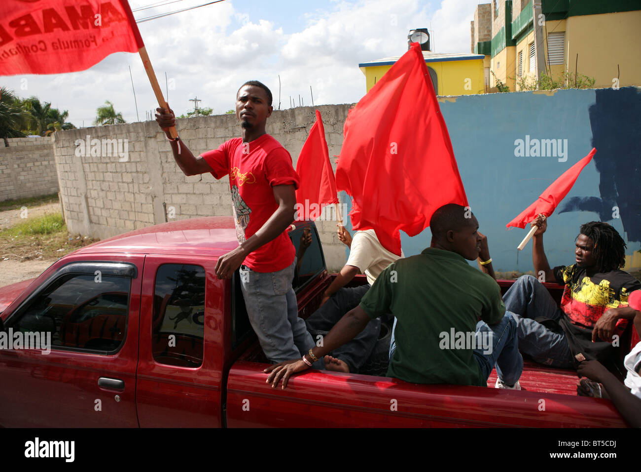 Group of young males travel in the back of a truck waving red flags on a political rally in the Dominican Republic Stock Photo