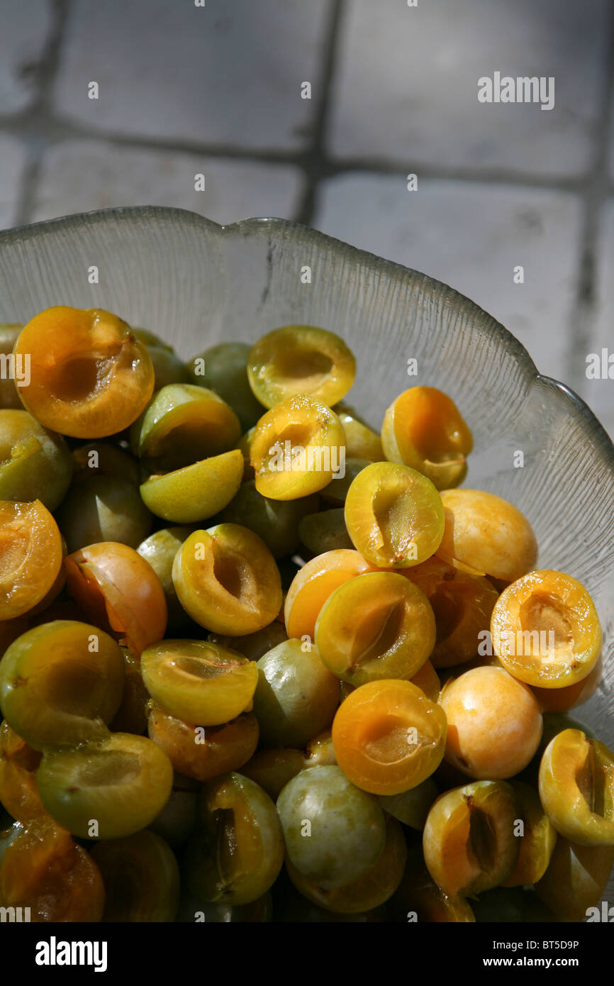 (Prunus x domestica var. syriaca) Halved and stoned Mirabelle plums in a glass bowl. Stock Photo
