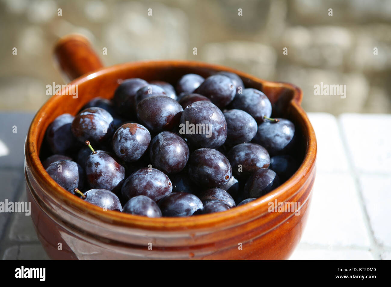 (Prunus domestica subsp. insititia) Freshly picked whole ripe damsons in a brown ceramic pot Stock Photo