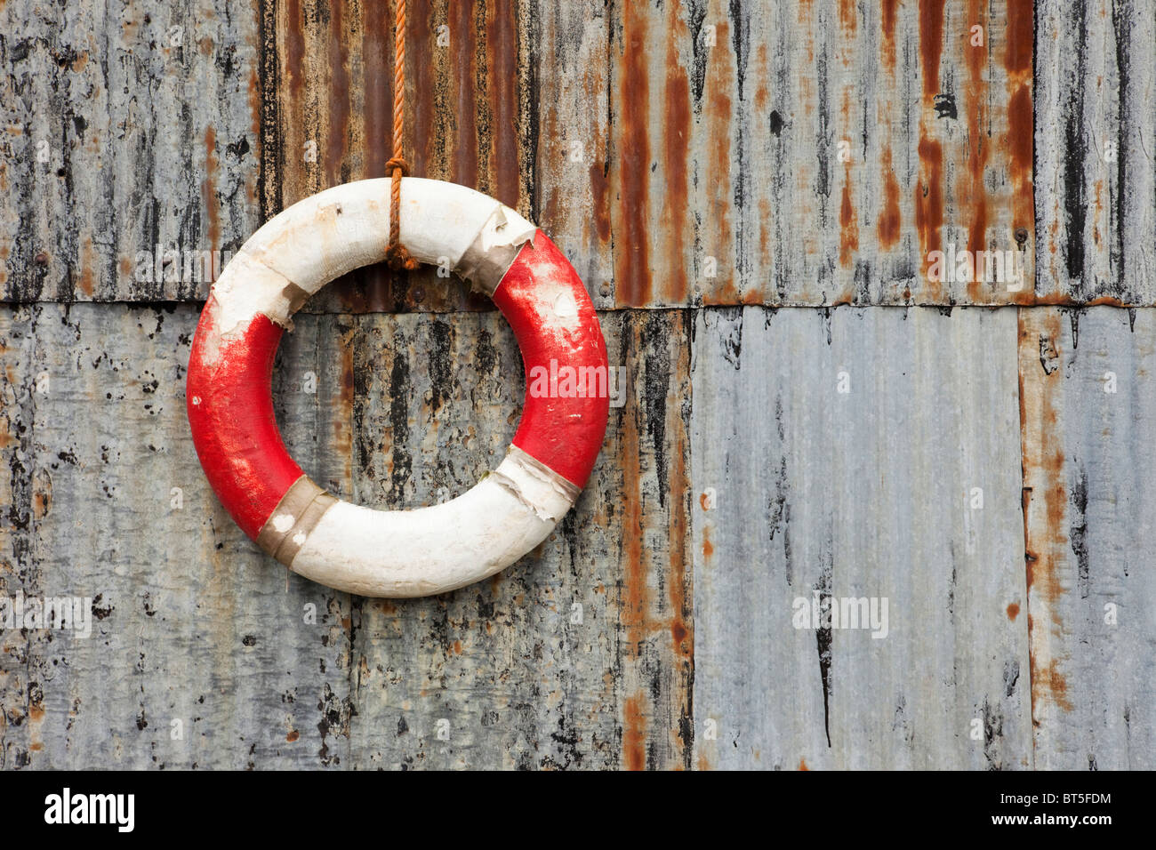 Old lifebuoy ring hanging on a corrugated iron rusty metal wall. UK Britain Stock Photo