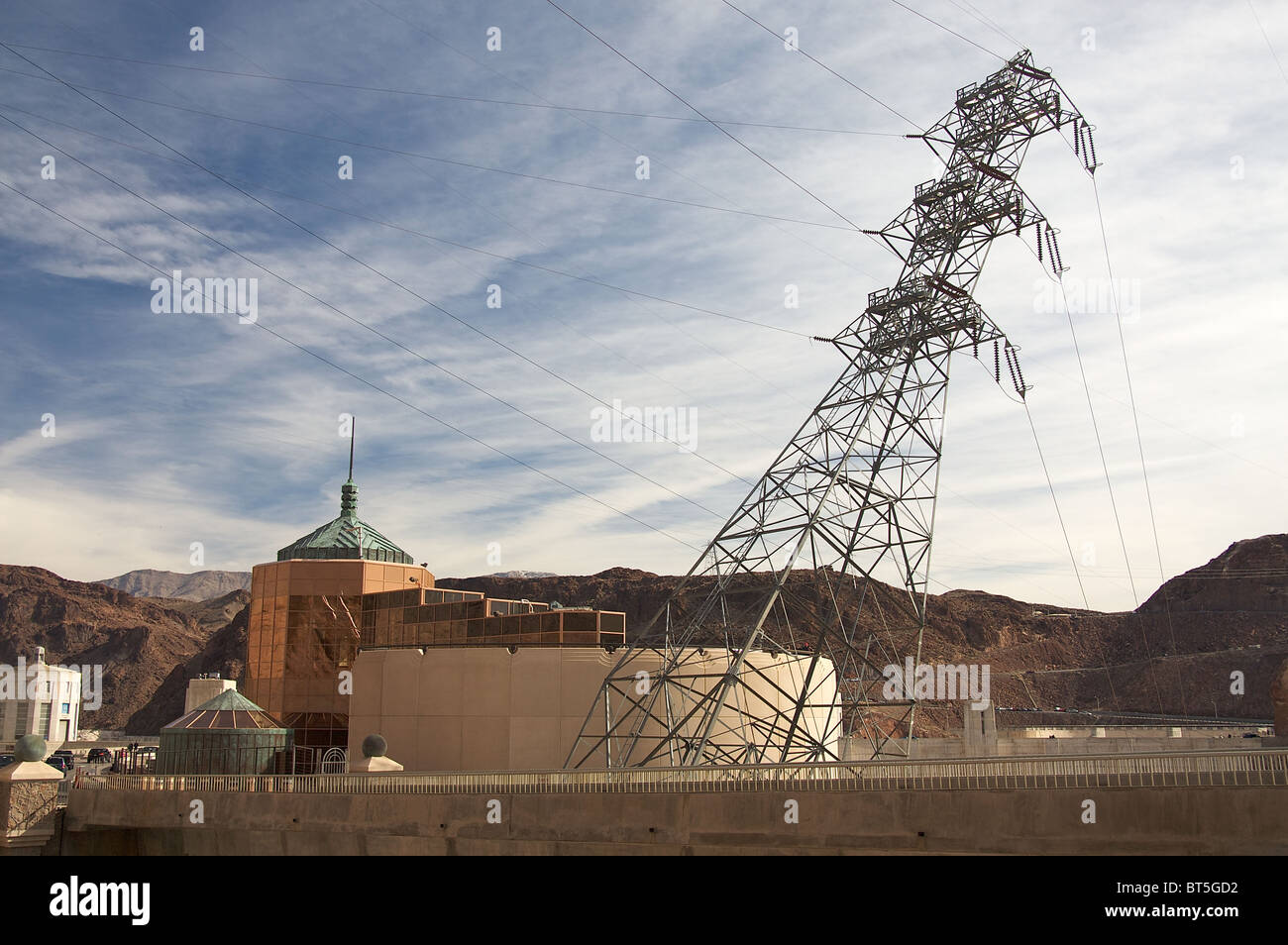 Power lines extend from an electrical pylon leaning over the highway near the Hoover Dam and its visitor's center. Stock Photo