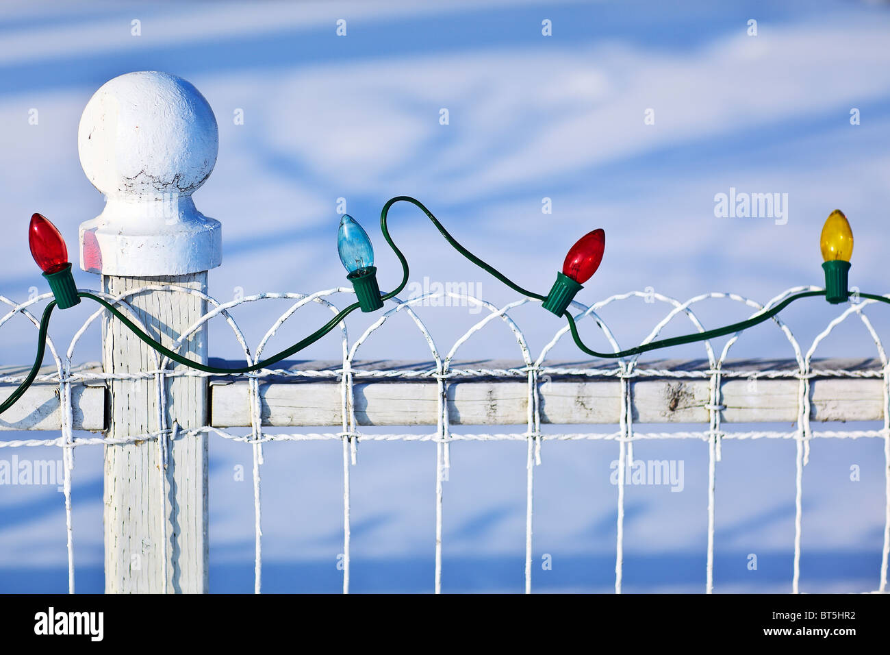 String of colored Christmas lights on a white fence, Gimli, Manitoba, Canada. Stock Photo