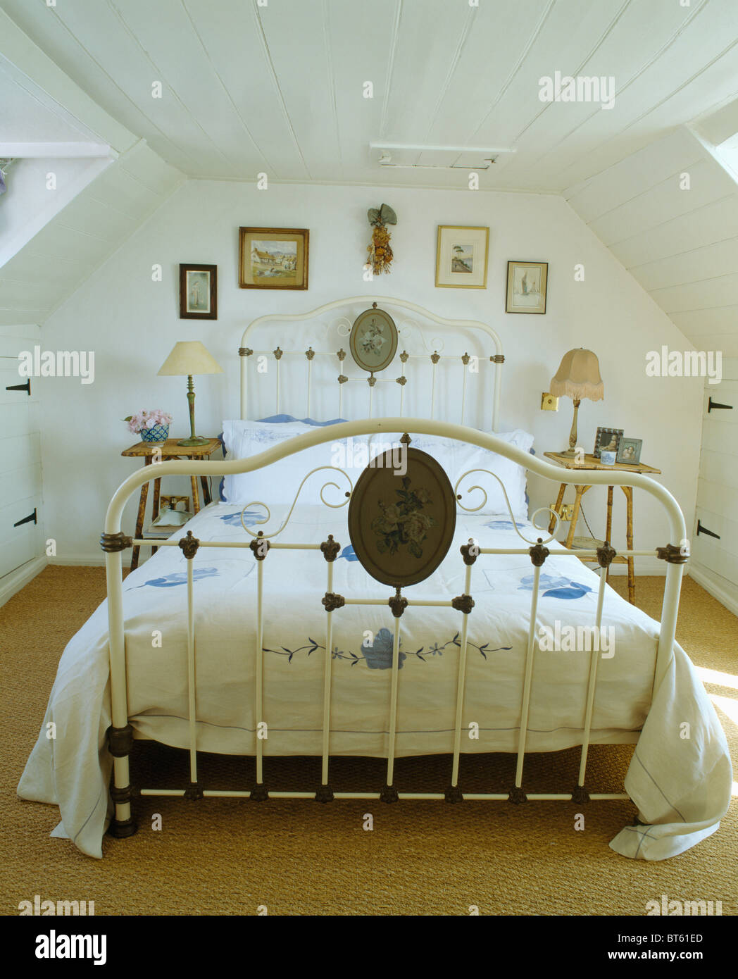 White wrought iron bed with blue+white quilt in white attic bedroom Stock Photo