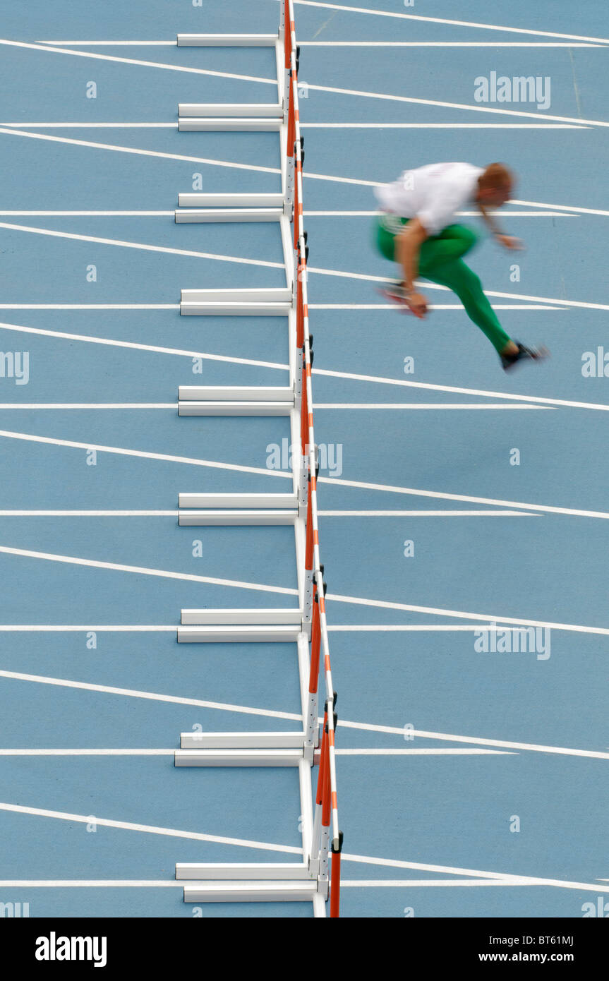 lone male sprinter jumps over hurdle during track and field event Stock