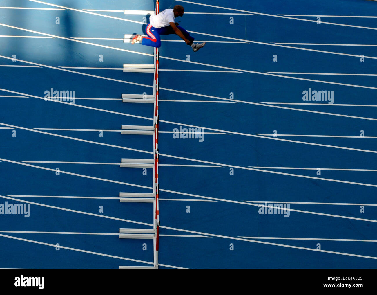 lone male sprinter jumps over hurdle during track and field event Stock