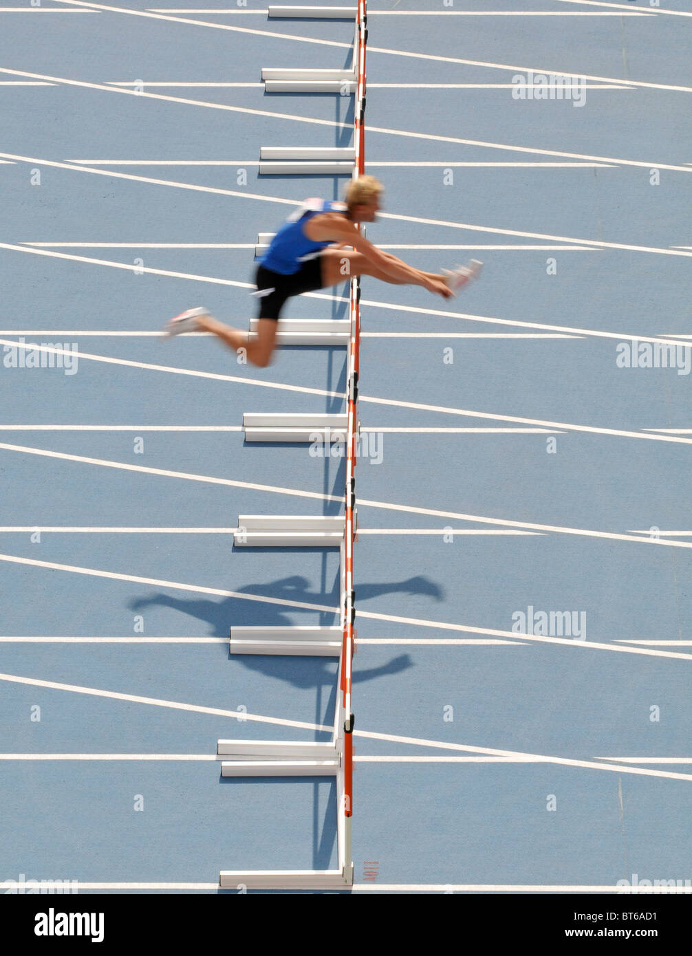 lone male sprinter jumps over hurdle during track and field event Stock Photo