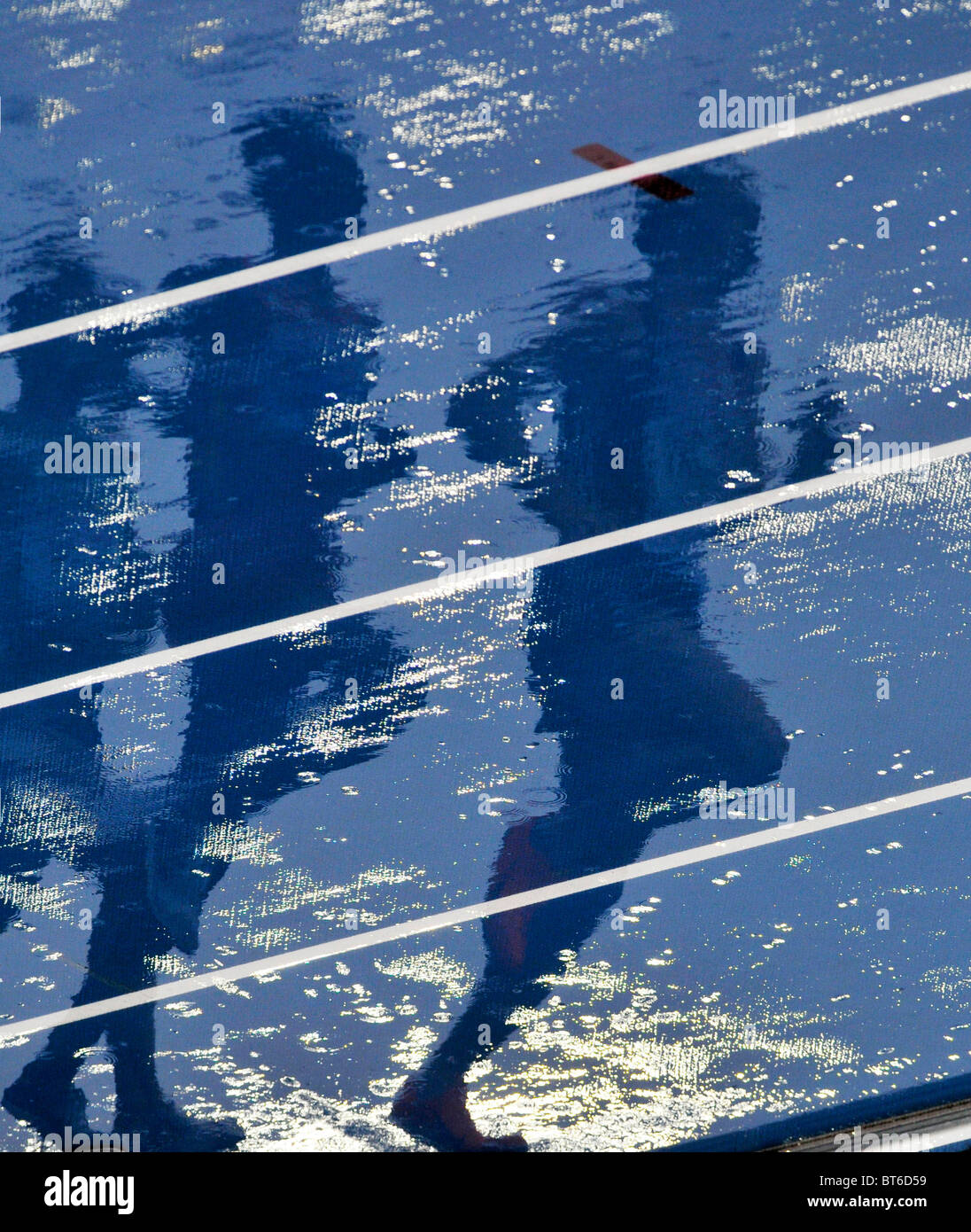 shadows of runners on blue running track covered in water Stock Photo