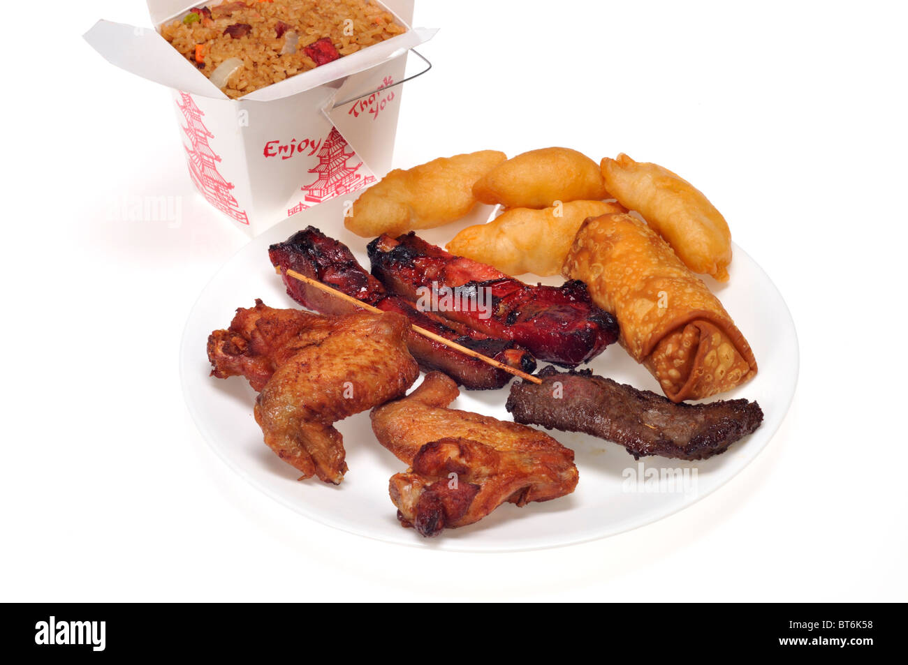 Plate with a chinese dinner of pork fried rice, chicken fingers & spare ribs and beef teriyaki stick with carton on white background. Stock Photo