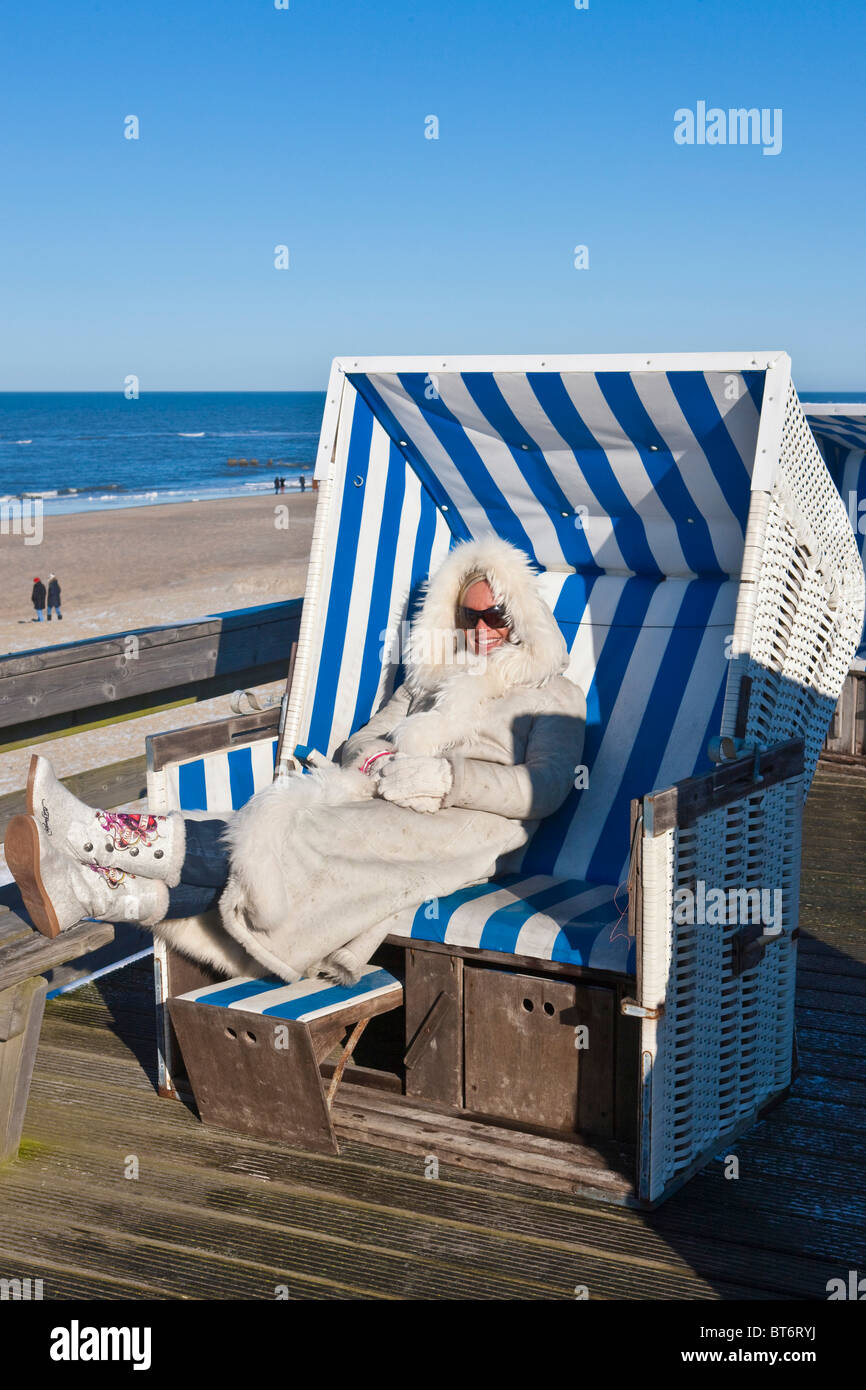 Woman wearing a fur coat sitting in a roofed wicker beach chair in winter at Rotes Kliff, Kampen