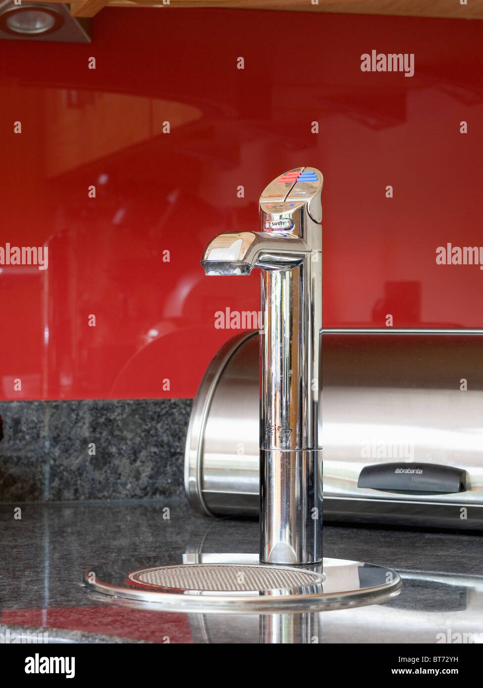 Close-up of modern stainless-steel tap against red kitchen wall Stock Photo