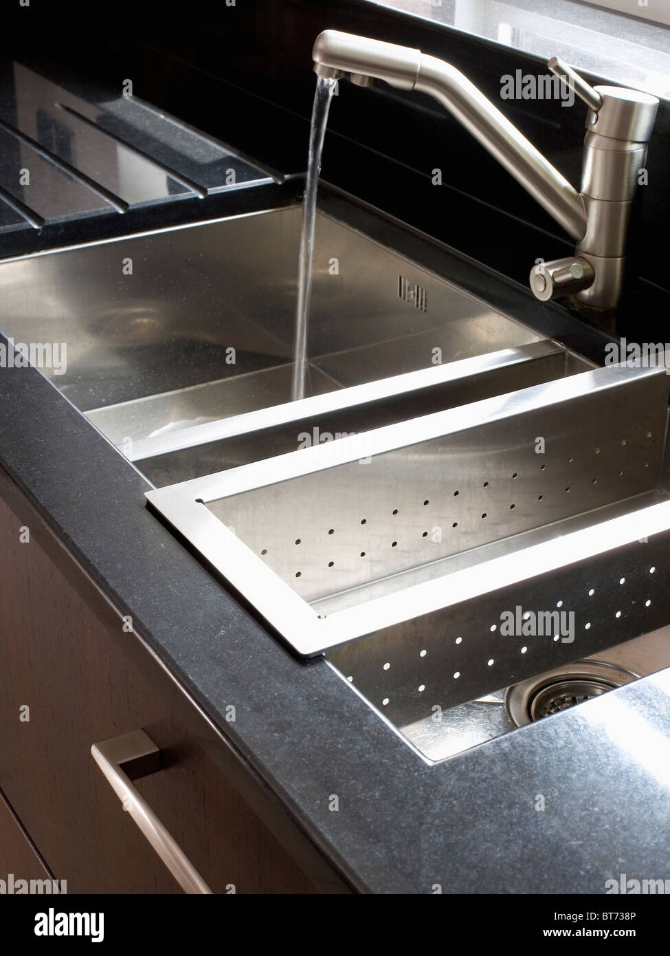 Close-up of tap pouring water into double stainless-steel sink with ...