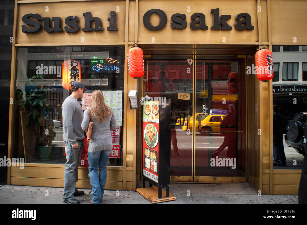 Passersby read the menu in the window of a Japanese sushi restaurant
