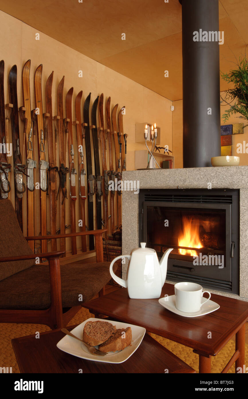 White ceramic teapot, cup and cookies on a table in front of a fireplace and a ski rack Stock Photo