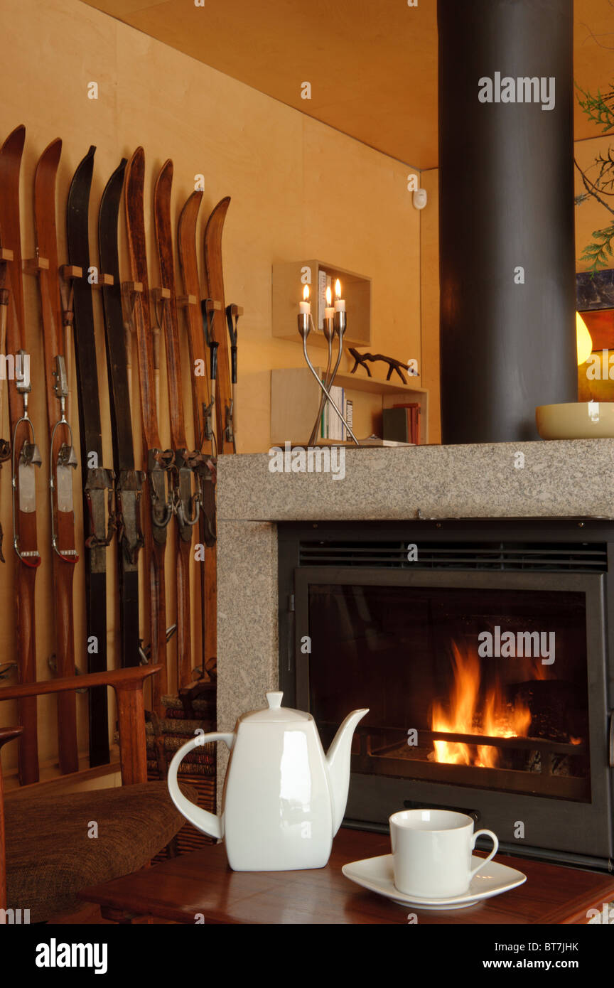 White ceramic teapot and cup on a table in front of a fireplace and a ski rack Stock Photo
