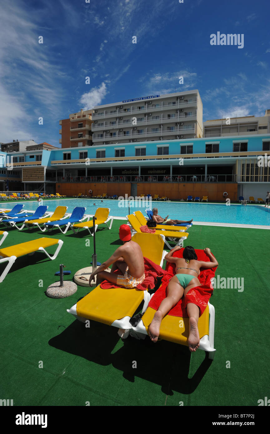 Group of people on lounge chairs sunbathing by a outdoor swimming pool