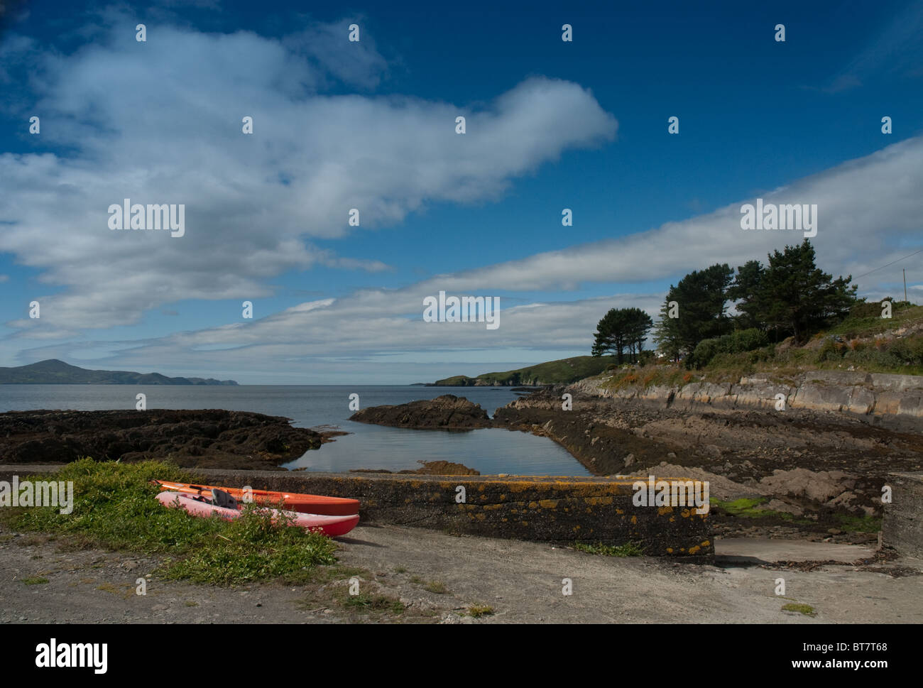 A small inlet, on a sunny day, with stone wall and two red canoes in front, in Reenmore, West Cork, Ireland Stock Photo