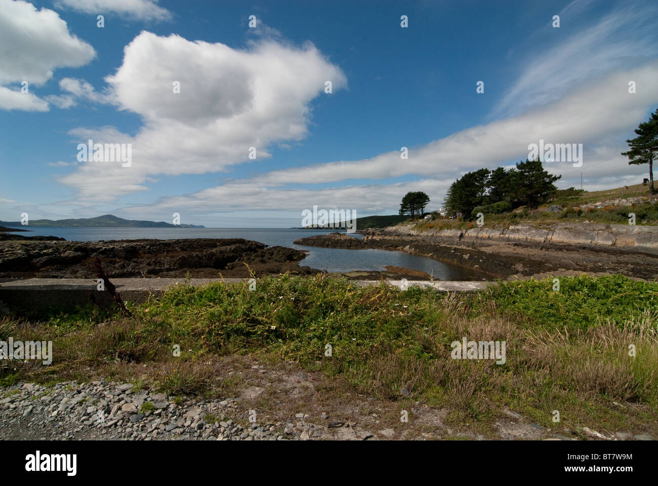 Reenmore beach, West Cork, Ireland. Small wall and greenery in front. with blue sky and wispy white clouds. Trees to right. Stock Photo
