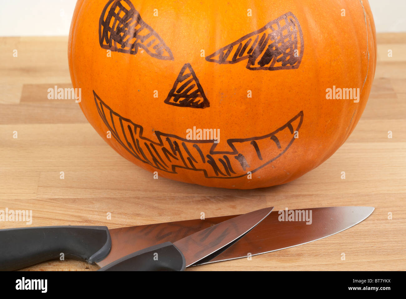 pumpkin ready to be turned into jack-o-lantern with cut outs drawn in pen with knives Stock Photo