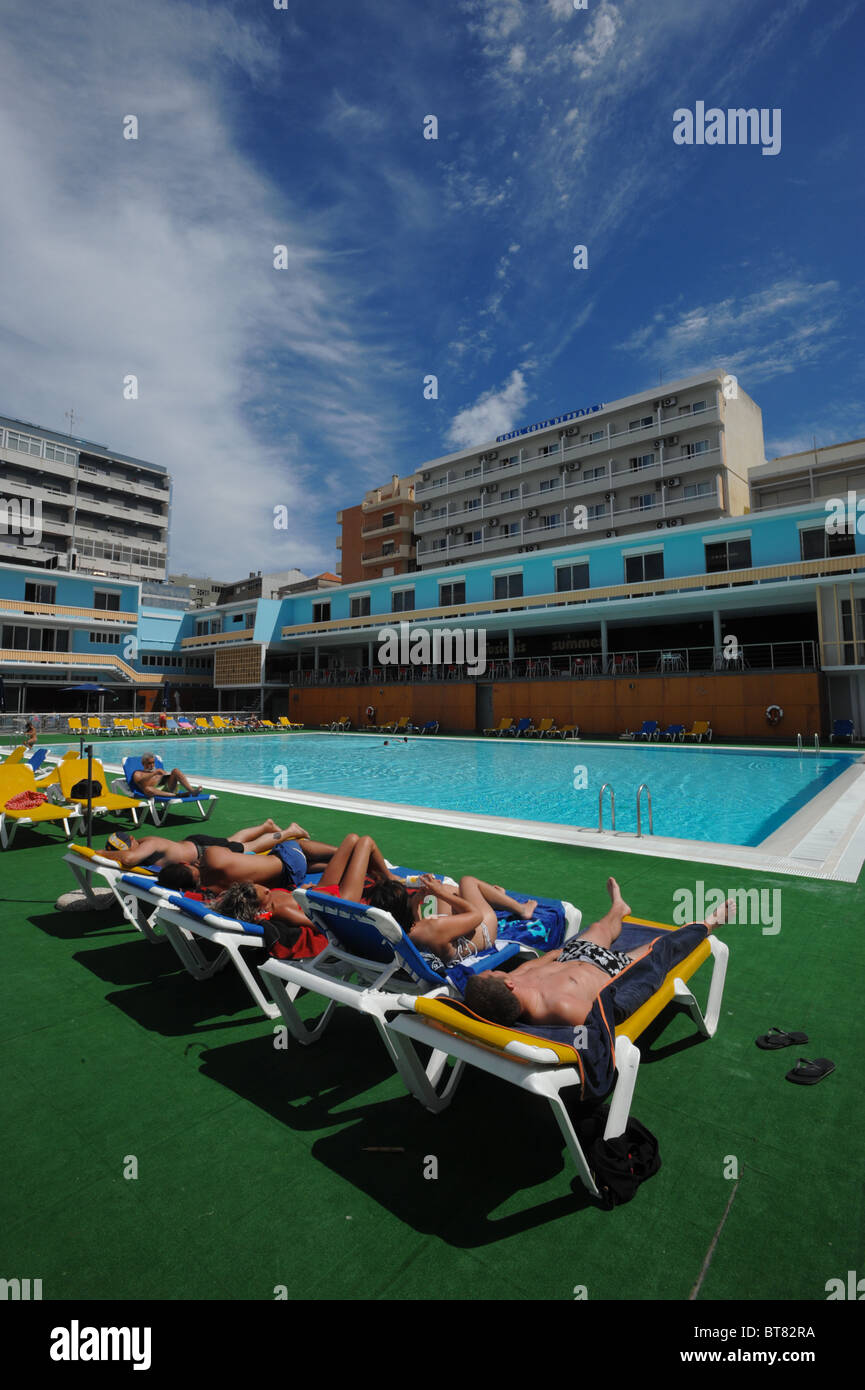 Group of people on lounge chairs sunbathing by a outdoor swimming pool
