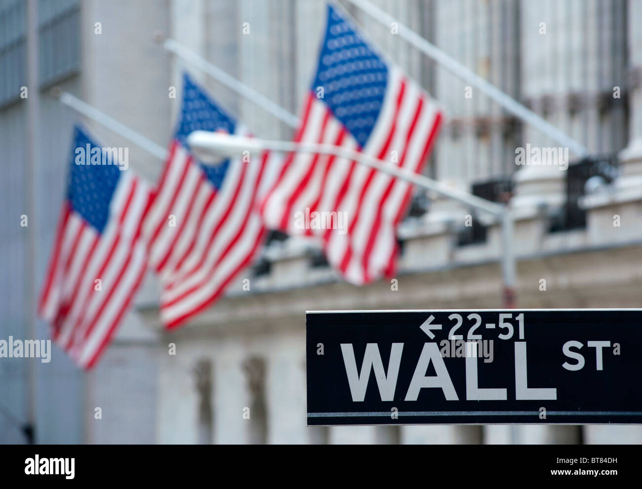 Detail of Wall Street sign with flags on Stock Exchange building to rear Manhattan New York City Stock Photo