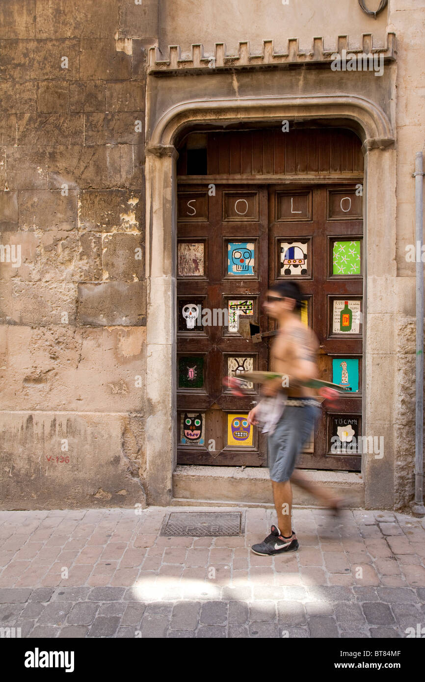 Spanish man with a skateboard in front of a door with artwork by Albert