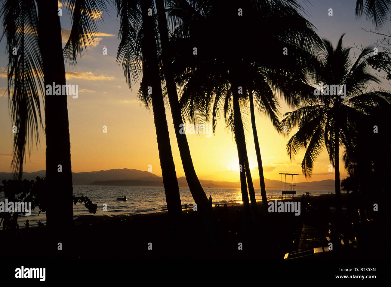 Beach with palm trees, sunset on the Pacific Coast in Puntarenas, Peninsula de Nicoya at back, Costa Rica, Pacific Ocean Stock Photo