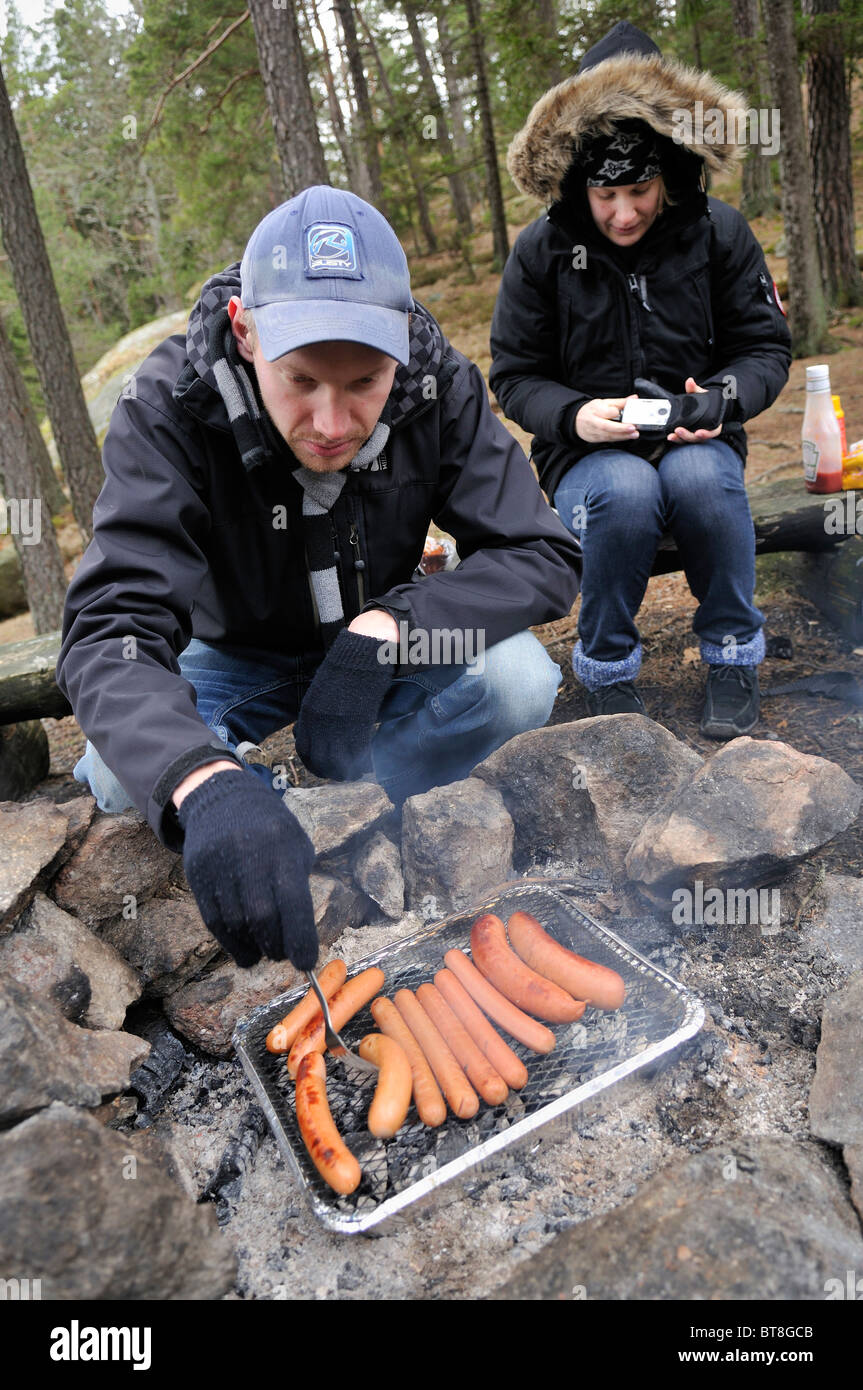 Man and woman barbecuing sausages in winter, Stockholms Lan, Sweden Stock Photo