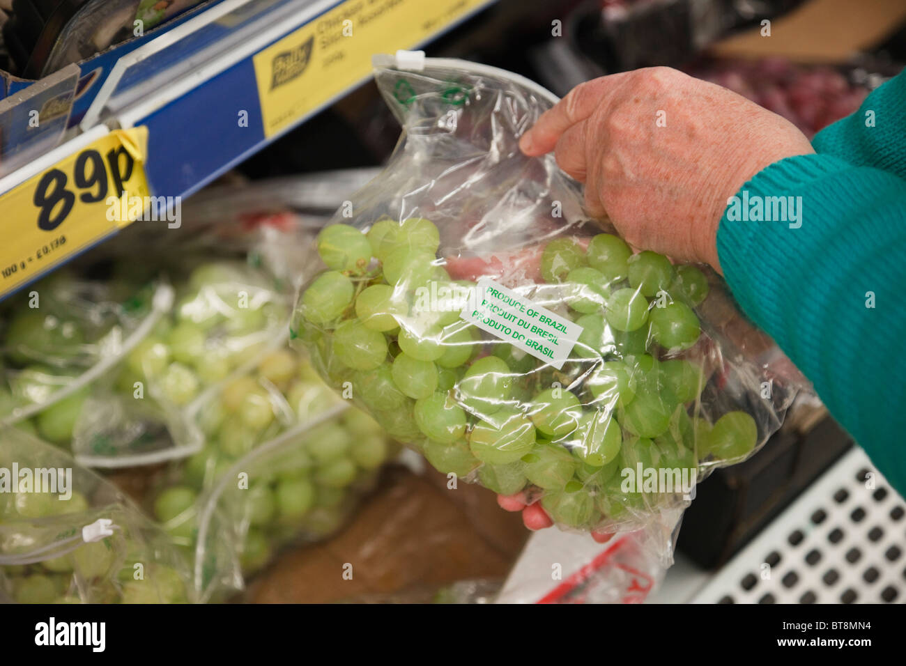 Woman choosing a packet of cheap priced grapes in a plastic bag displayed on a Lidl supermarket shelf. UK Britain Stock Photo