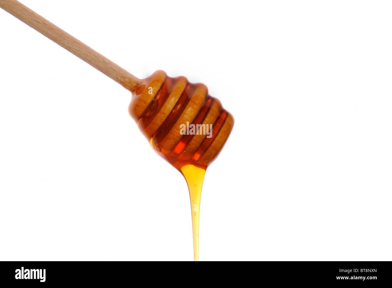 Wooden honey drizzle with honey running off against white background