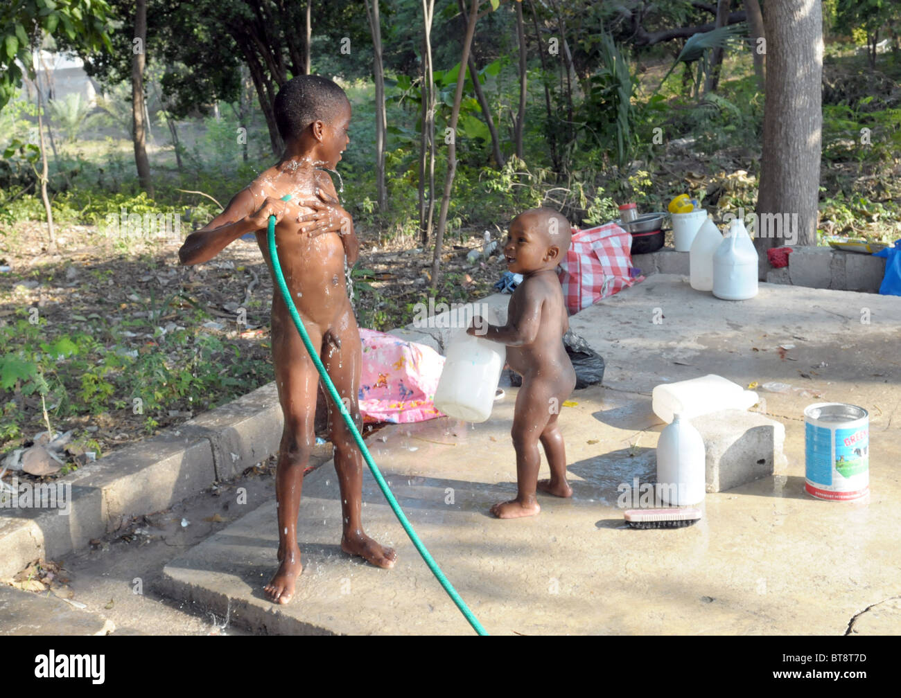 Haitian children washing themselves outdoors with a hose pipe Stock Photo