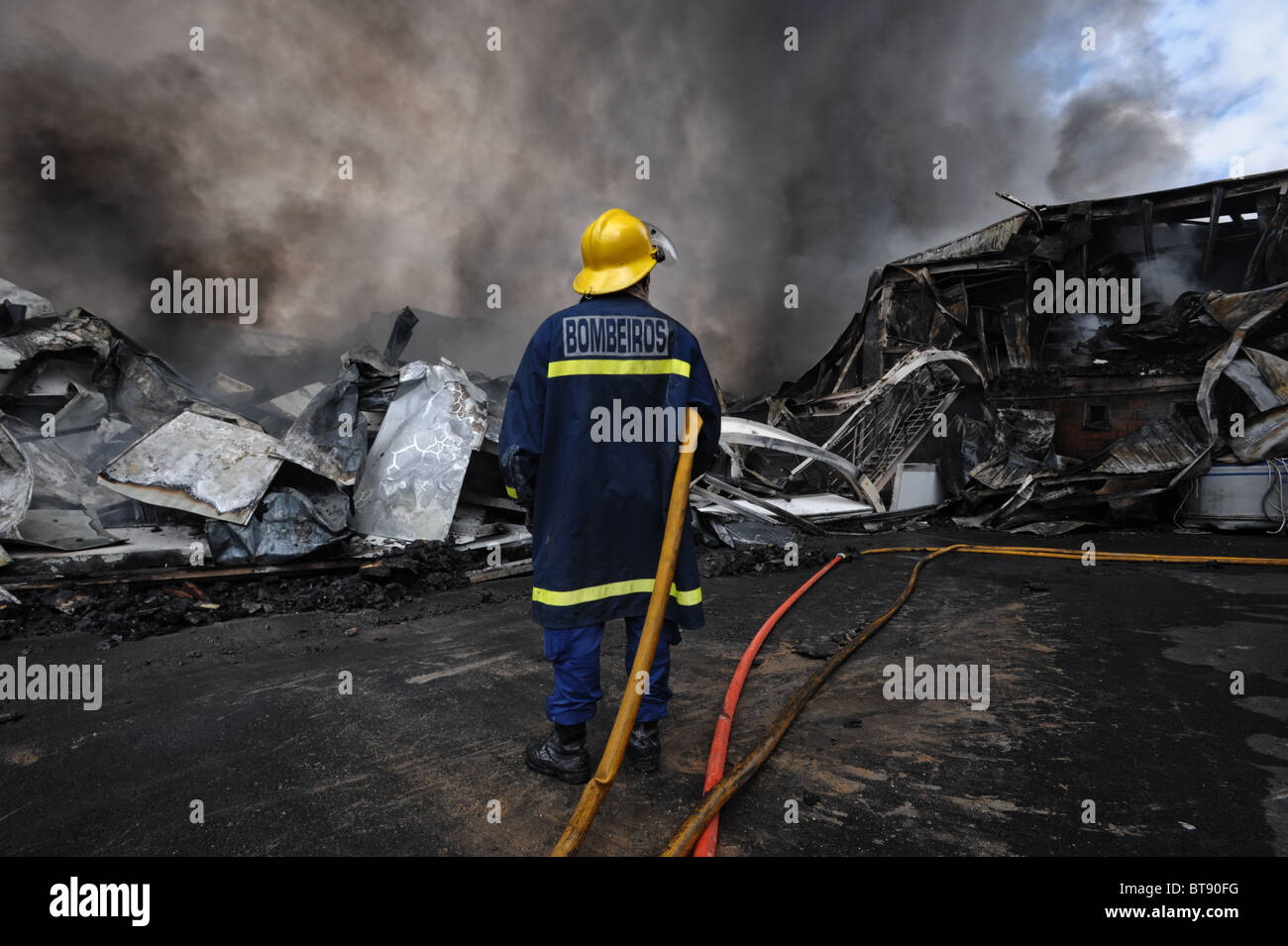 Lone fireman looks helplessly at the remains of a factory building burnt down by a massive fire Stock Photo