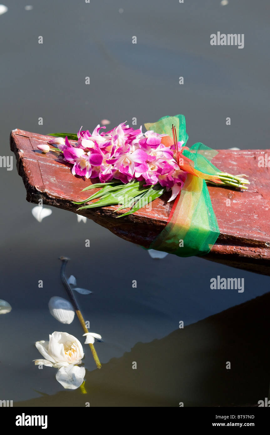 Orchids on an old wooden boat in Thailand with fragments of lotus flowers floating in the water. Stock Photo